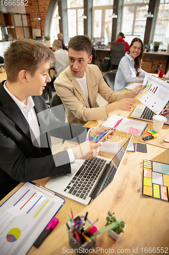 Image of Young caucasian colleagues working together in a office using modern devices and gadgets