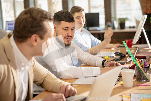 Image of Young caucasian colleagues working together in a office using modern devices and gadgets