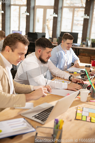 Image of Young caucasian colleagues working together in a office using modern devices and gadgets