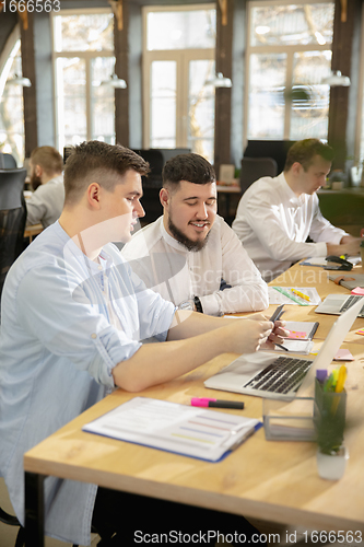 Image of Young caucasian colleagues working together in a office using modern devices and gadgets