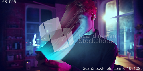 Image of Cinematic portrait of stylish man in neon lighted interior using a smartphone. The face is smeared, sucked into the phone. The concept of social network dependency