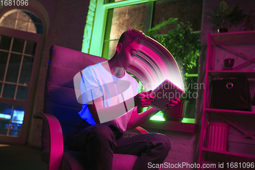 Image of Cinematic portrait of stylish woman in neon lighted interior using a tablet. The face is smeared, sucked into the screen. The concept of social network dependency