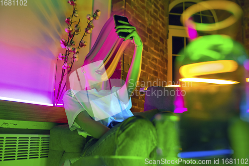 Image of Cinematic portrait of stylish woman in neon lighted interior using a smartphone. The face is smeared, sucked into the phone. The concept of social network dependency