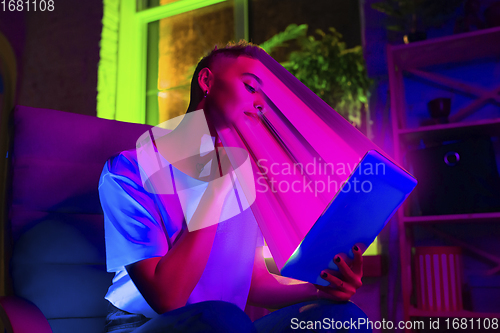 Image of Cinematic portrait of stylish woman in neon lighted interior using a tablet. The face is smeared, sucked into the screen. The concept of social network dependency