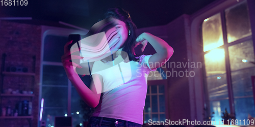 Image of Cinematic portrait of stylish woman in neon lighted interior using a smartphone. The face is smeared, sucked into the phone. The concept of social network dependency