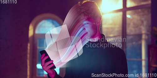 Image of Cinematic portrait of stylish man in neon lighted interior using a smartphone. The face is smeared, sucked into the phone. The concept of social network dependency