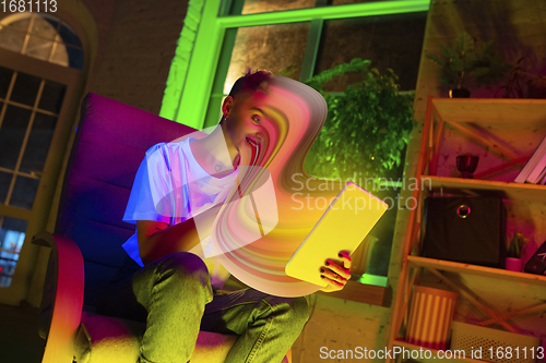 Image of Cinematic portrait of stylish woman in neon lighted interior using a tablet. The face is smeared, sucked into the screen. The concept of social network dependency