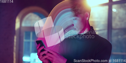 Image of Cinematic portrait of stylish man in neon lighted interior using a smartphone. The face is smeared, sucked into the screen. The concept of social network dependency