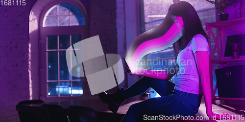 Image of Cinematic portrait of stylish woman in neon lighted interior using a smartphone. The face is smeared, sucked into the screen. The concept of social network dependency