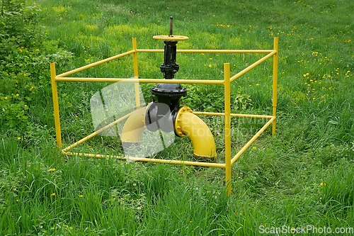 Image of Large gas valve outside among green grass and bushes