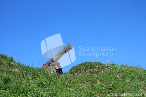 Image of Old black cannon in wooden base on green grass hill on the backg