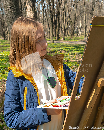 Image of Beautiful young girl painted on an easel in park