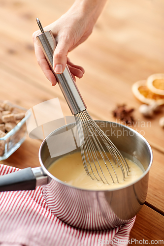 Image of close up of hand with whisk stirring eggnog in pot