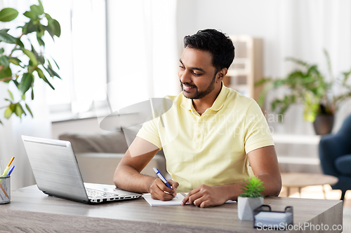 Image of indian man with notebook and laptop at home office