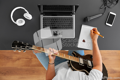 Image of man with guitar writing to music book at table