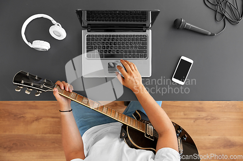 Image of young man with laptop playing guitar at table