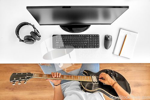 Image of young man with computer playing guitar at table