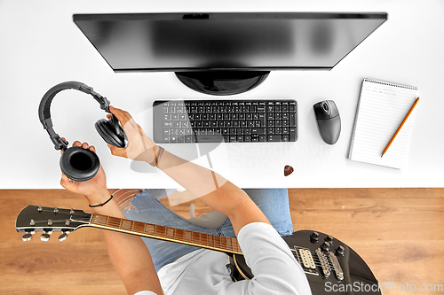 Image of young man with headphones and guitar at table