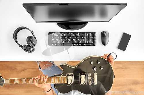 Image of young man with computer tuning guitar at table