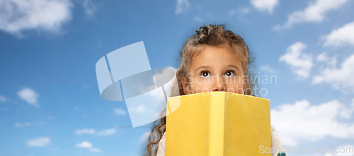 Image of little girl hiding behind book over sky and clouds