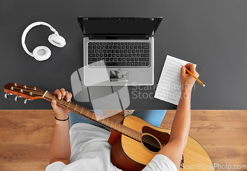 Image of man with guitar writing to music book at table