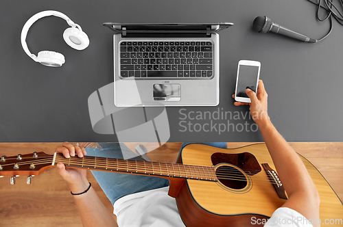 Image of young man with guitar and smartphone at table