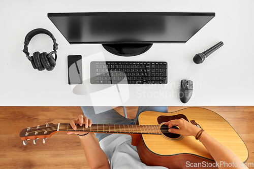 Image of young man with computer playing guitar at table