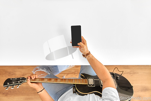 Image of young man with guitar and smartphone at table