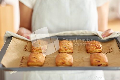 Image of woman holding baking tray with pies at kitchen