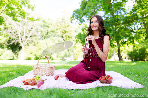 Image of happy woman with picnic basket and drink at park