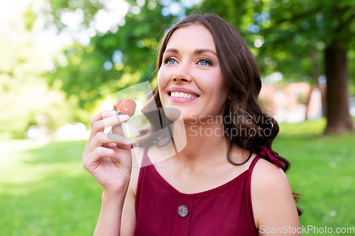 Image of happy woman eating strawberry at summer park