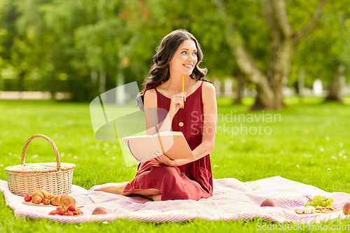 Image of happy woman with diary and picnic basket at park