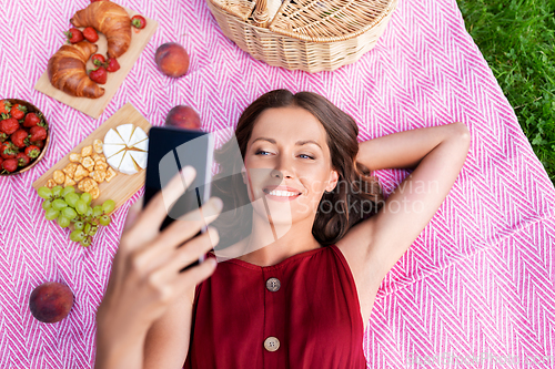 Image of happy woman with smartphone taking selfie at park