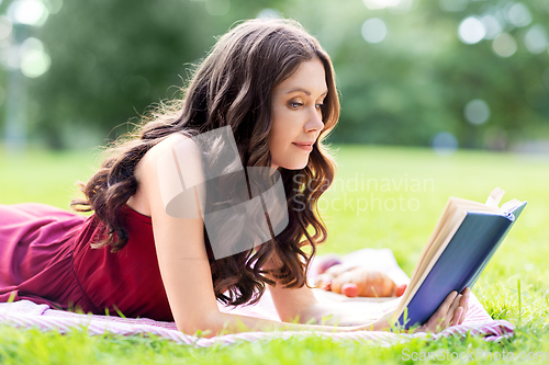 Image of happy young woman reading book at summer park