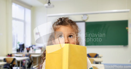 Image of little girl hiding behind yellow book at school