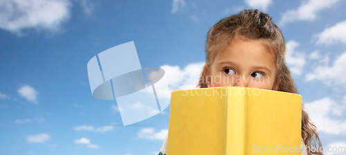 Image of little girl hiding behind book over sky and clouds
