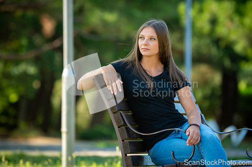 Image of A beautiful girl in casual clothes sits on a bench in a beautiful green park