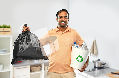 Image of smiling indian man sorting paper and plastic waste