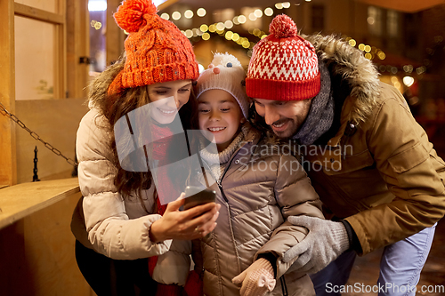 Image of happy family with smartphone at christmas market