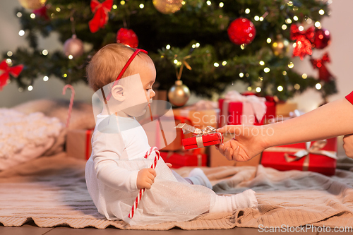 Image of baby girl at christmas tree with gifts at home