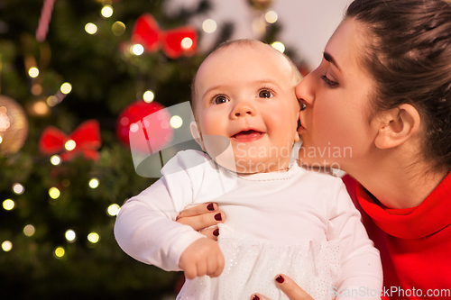 Image of mother kissing baby daughter over christmas tree