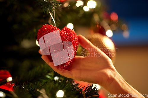 Image of hands decorating christmas tree with red heart