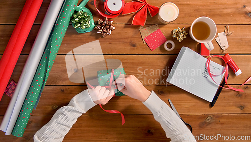Image of hands packing christmas gift and tying ribbon