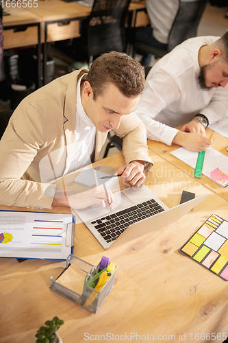 Image of Young caucasian colleagues working together in a office using modern devices and gadgets