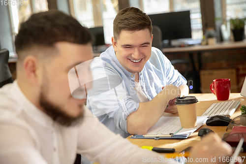 Image of Young caucasian colleagues working together in a office using modern devices and gadgets
