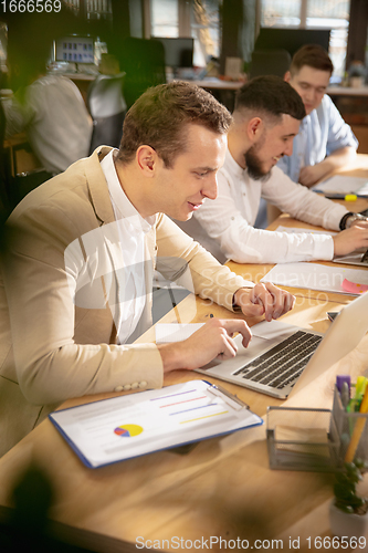 Image of Young caucasian colleagues working together in a office using modern devices and gadgets