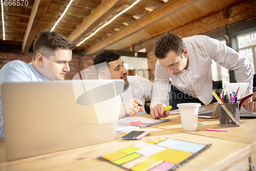 Image of Young caucasian colleagues working together in a office using modern devices and gadgets