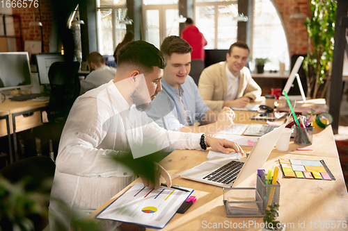 Image of Young caucasian colleagues working together in a office using modern devices and gadgets