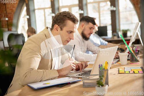 Image of Young caucasian colleagues working together in a office using modern devices and gadgets