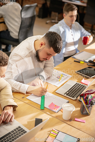 Image of Young caucasian colleagues working together in a office using modern devices and gadgets